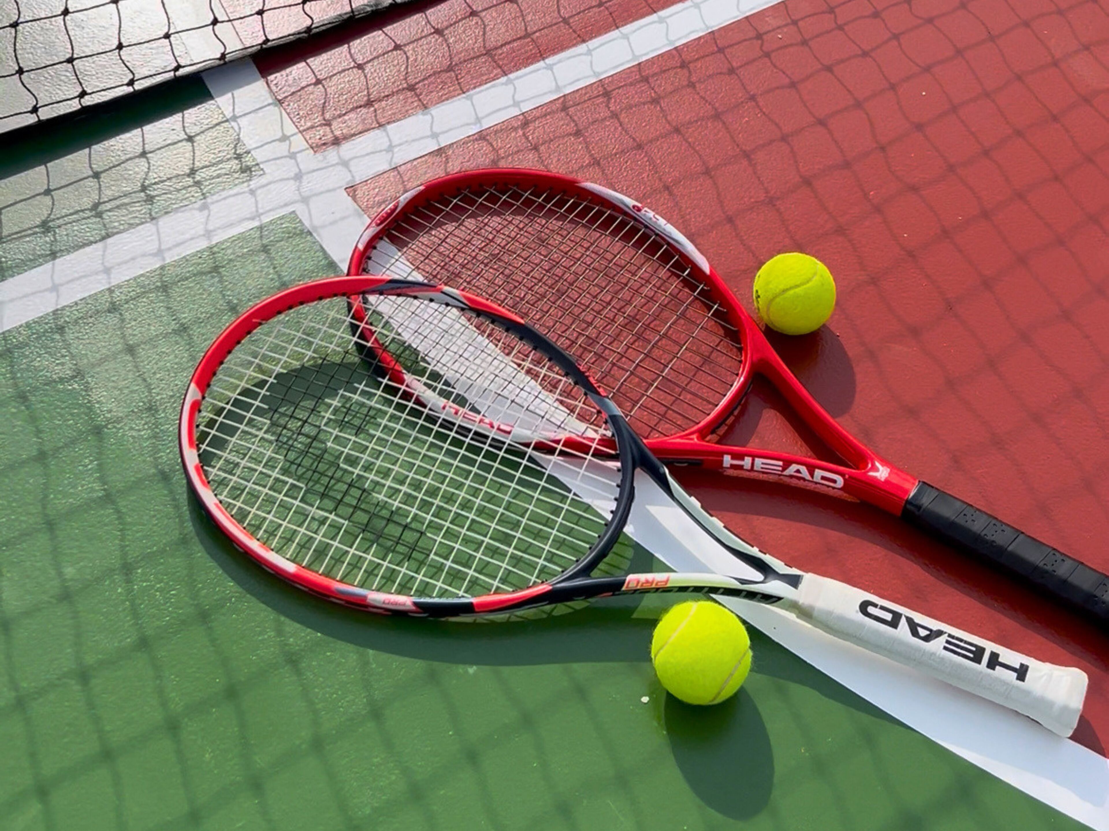 Two tennis rackets and three tennis balls on a court.