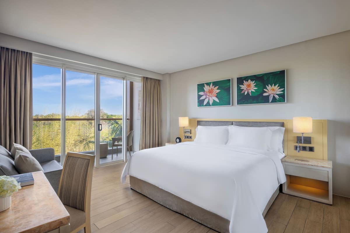 Ein Hotelzimmer mit einem großen Bett, einem Schreibtisch mit Stuhl, einem Balkon mit Vorhängen und zwei Wandlampen.