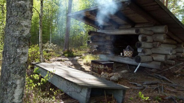 A rustic cabin with a chimney emitting smoke, surrounded by a forest. - Salkolahti Tikkamaki (Orivesi)