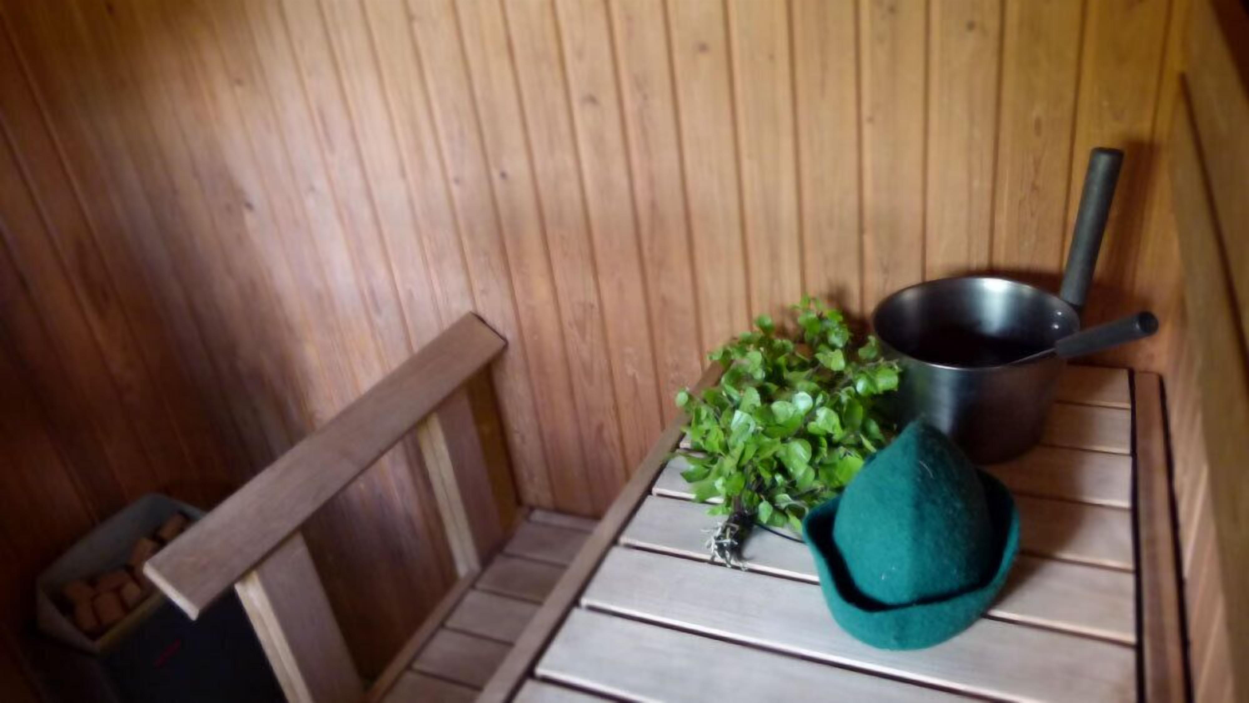 A wooden sauna with a bench, a small plant, and a metal pot.