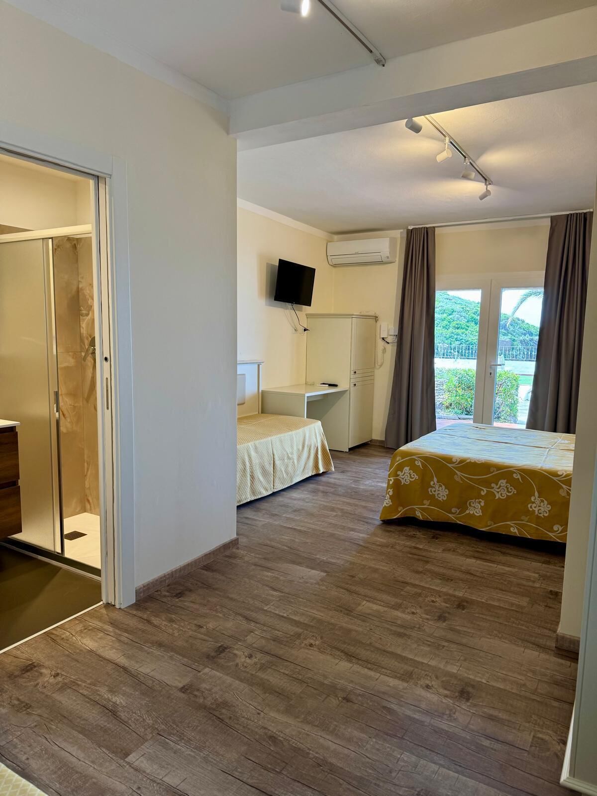 Een hotelkamer met een bed, bureau, televisie en een balkon met gordijnen.