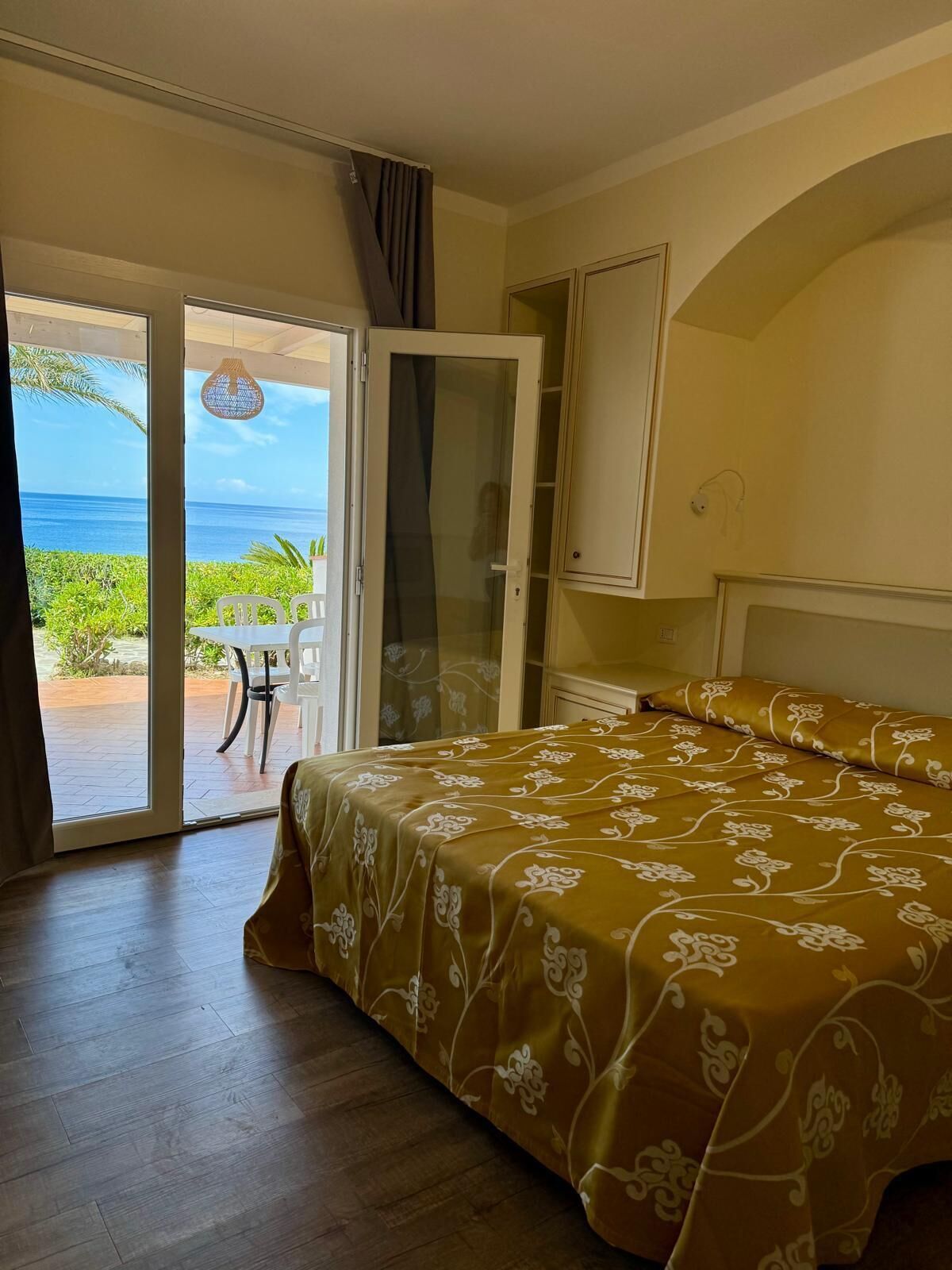 A bedroom with a bed, a sliding glass door leading to a balcony, and a view of the ocean.