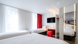 A hotel room with two beds, a desk, a red chair, and a TV mounted on the wall.