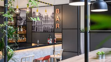 A bar area with a counter, two chairs, hanging lights, and a wall-mounted sign.