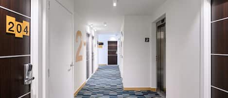 Un pasillo de hotel con alfombra estampada, puertas numeradas y un ascensor.