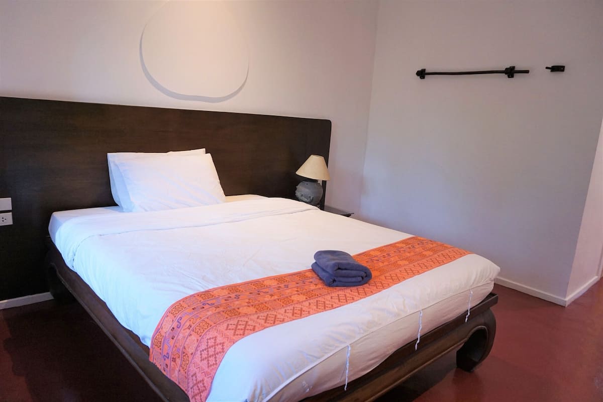 A neatly made bed with a white and orange patterned blanket, a pillow, and a folded towel on the bed.