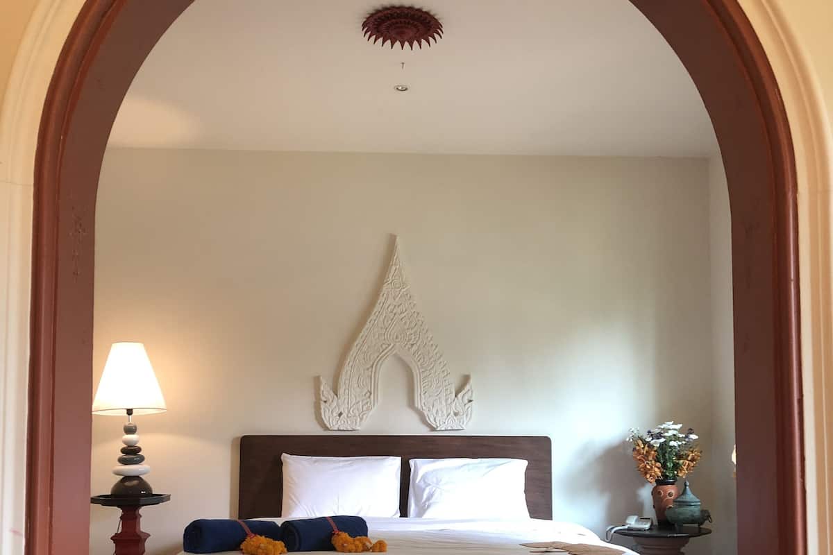 A hotel room with a large bed, a decorative wall piece above the bed, a bedside table with a lamp, and a vase with flowers.