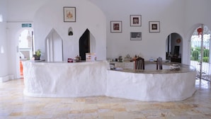 A reception area with a curved white counter, framed artwork on the walls, and a tiled floor. - Amaravati Wellness Center and Resort (Mae Rim)