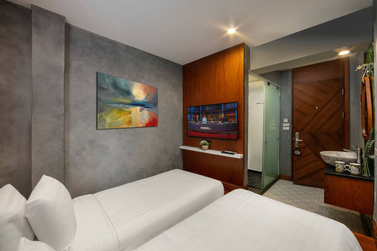 A hotel room with two beds, a TV, a painting, and a wooden wardrobe.