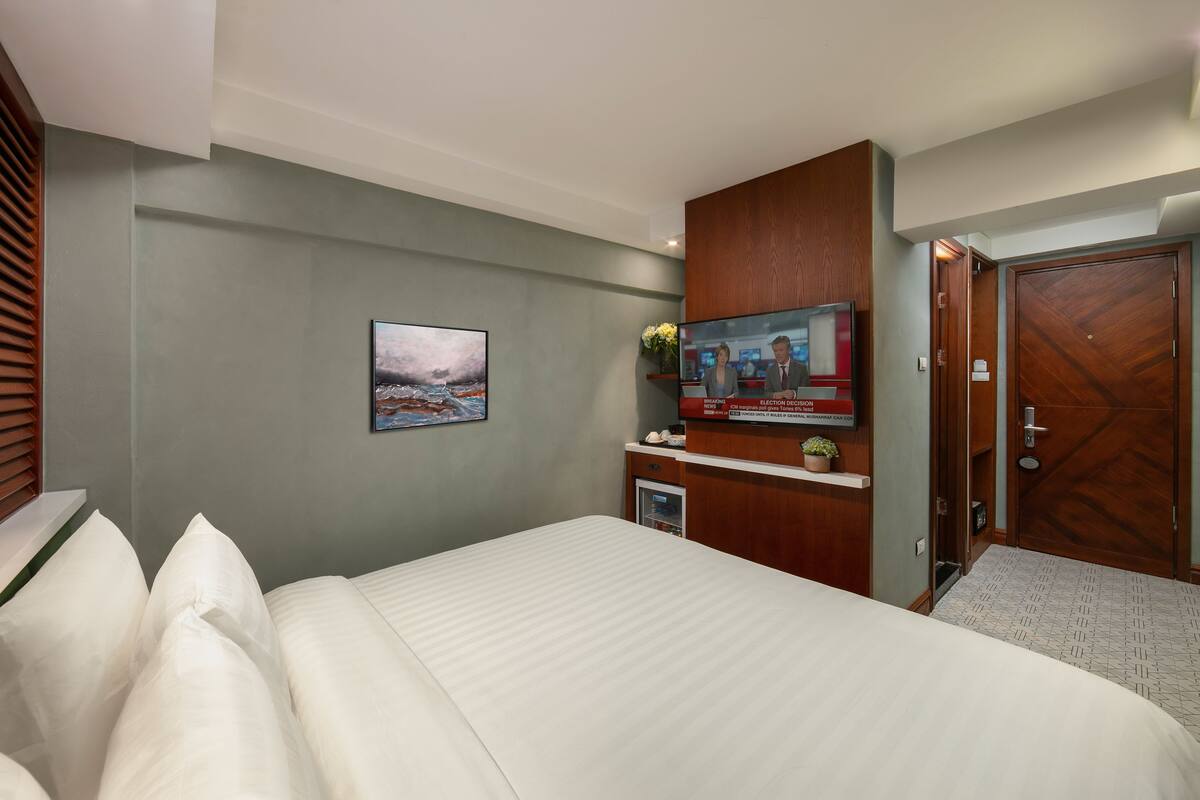 A hotel room with a large bed, a television, a small desk with a computer, a framed picture on the wall, and a wooden wardrobe.