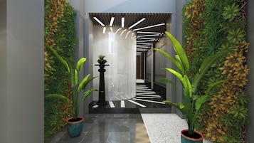 A modern hallway with a curved ceiling, black and white patterned floor, and green plants on either side.