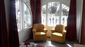 A room with two yellow armchairs, a large arched window, and a view of a courtyard. - Valentino Bed & Breakfast (Fuengirola)