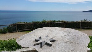 A stone monument with inscriptions and a star-shaped design, surrounded by a wooden fence and greenery, overlooking a body of water. - Villaggio Innamorata - Villa Quintavalle (Capoliveri)