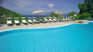 A poolside area with lounge chairs and umbrellas, a clear blue pool, and a view of the sea. - Villaggio Innamorata - Villa Quintavalle (Capoliveri)