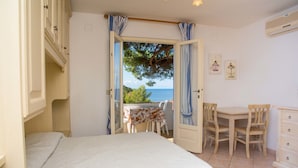 Una camera da letto con un letto, un tavolo e sedie, vista mare attraverso una porta aperta e un piccolo balcone con tavolo e sedie.
