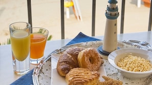 Un vassoio da colazione con croissant, un modellino di faro e una ciotola di mais sulla spiaggia, con vista sull'oceano e ombrelloni.