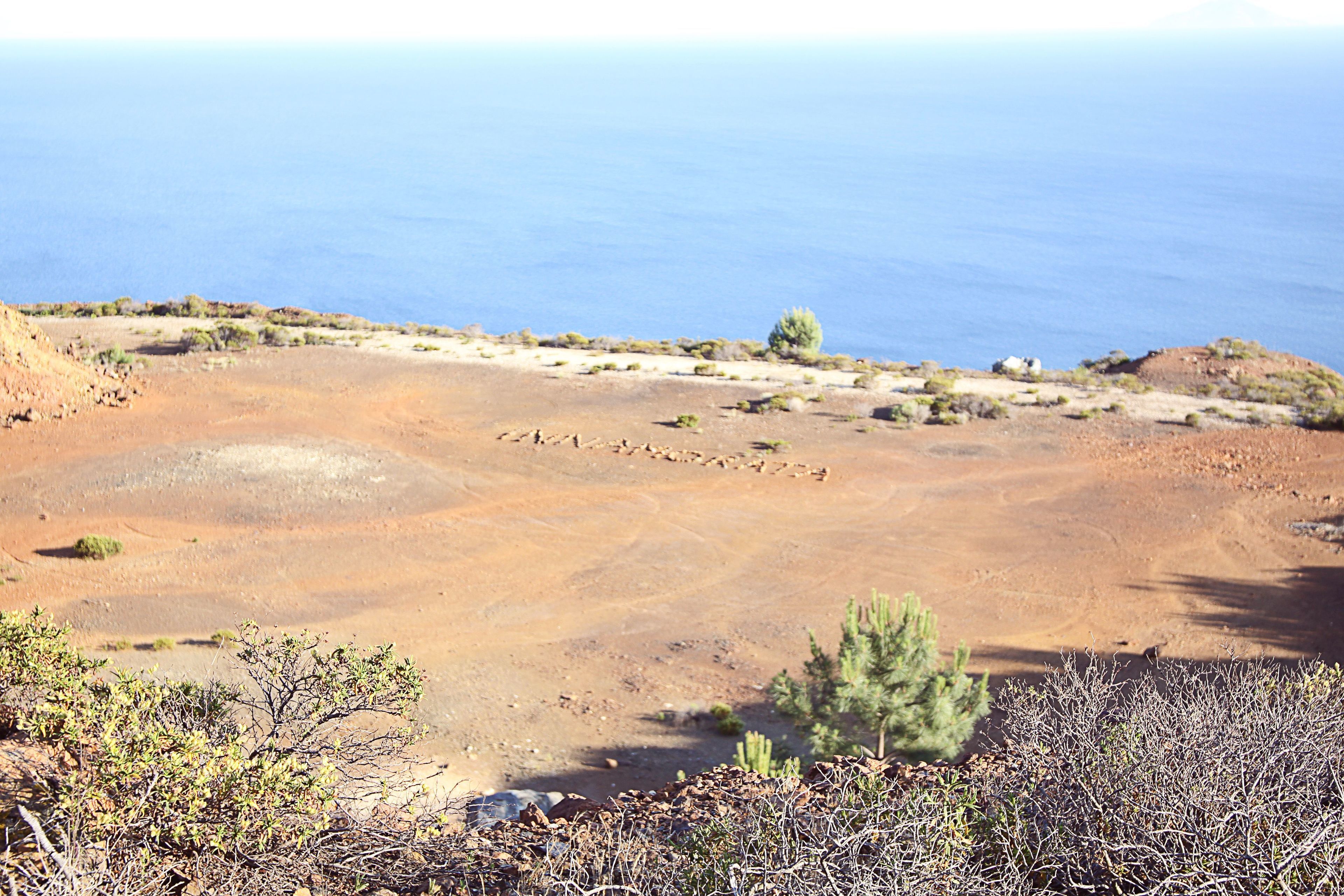 Eine karge Landschaft mit vereinzelter Vegetation und freiem Blick auf das Meer.