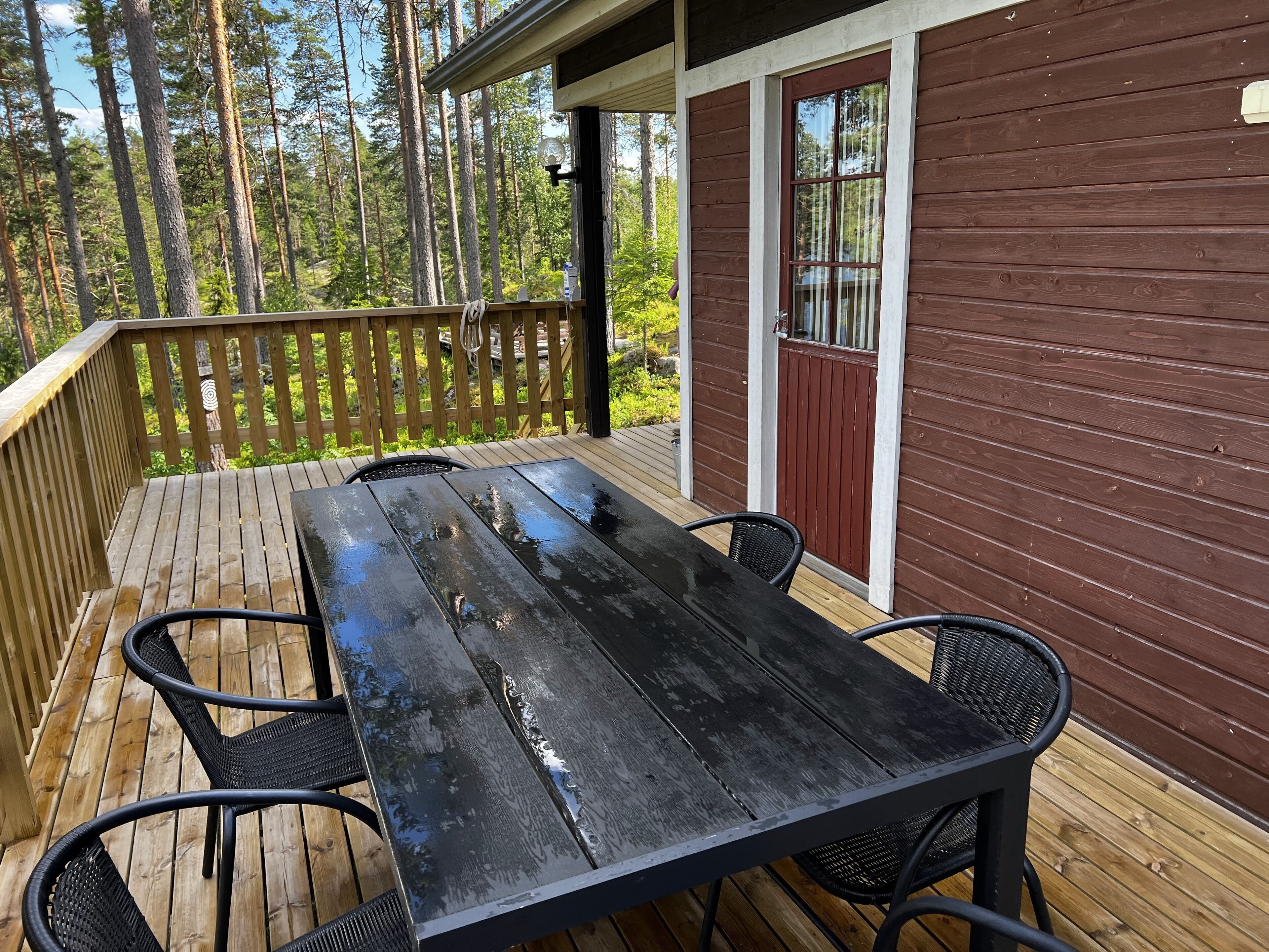 A wooden deck with a table and chairs, a railing, and a building with a brown exterior and a window.