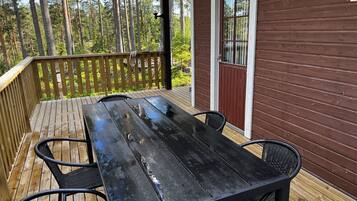A wooden deck with a table and chairs, a railing, and a building with a brown exterior and a window.