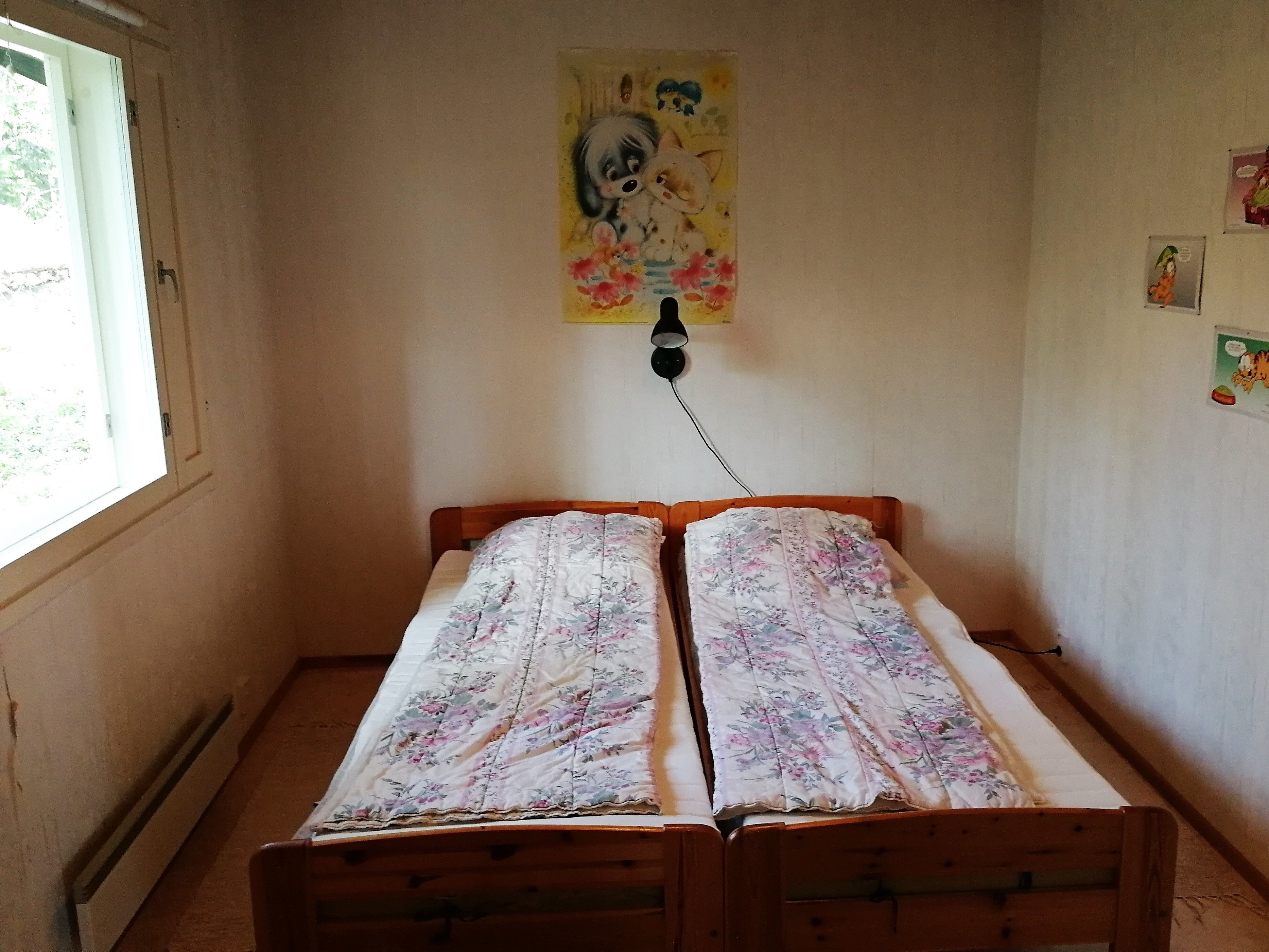 Een kleine kamer met een enkel bed, een raam en een lamp aan de muur.