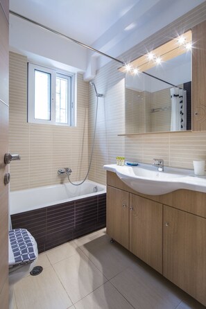 A modern bathroom with a bathtub, a shower, and a vanity with a mirror. - Scorpio Deluxe Apartment with Private Garden (Glyfada)