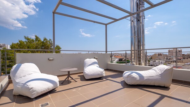 Una terraza en la azotea con dos sillones colgantes blancos y una pequeña mesa redonda, con vistas despejadas del paisaje urbano.