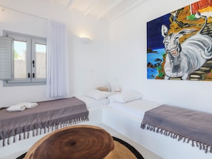 Una habitación con dos camas, un cuadro, una ventana con cortinas y una mesa de madera.