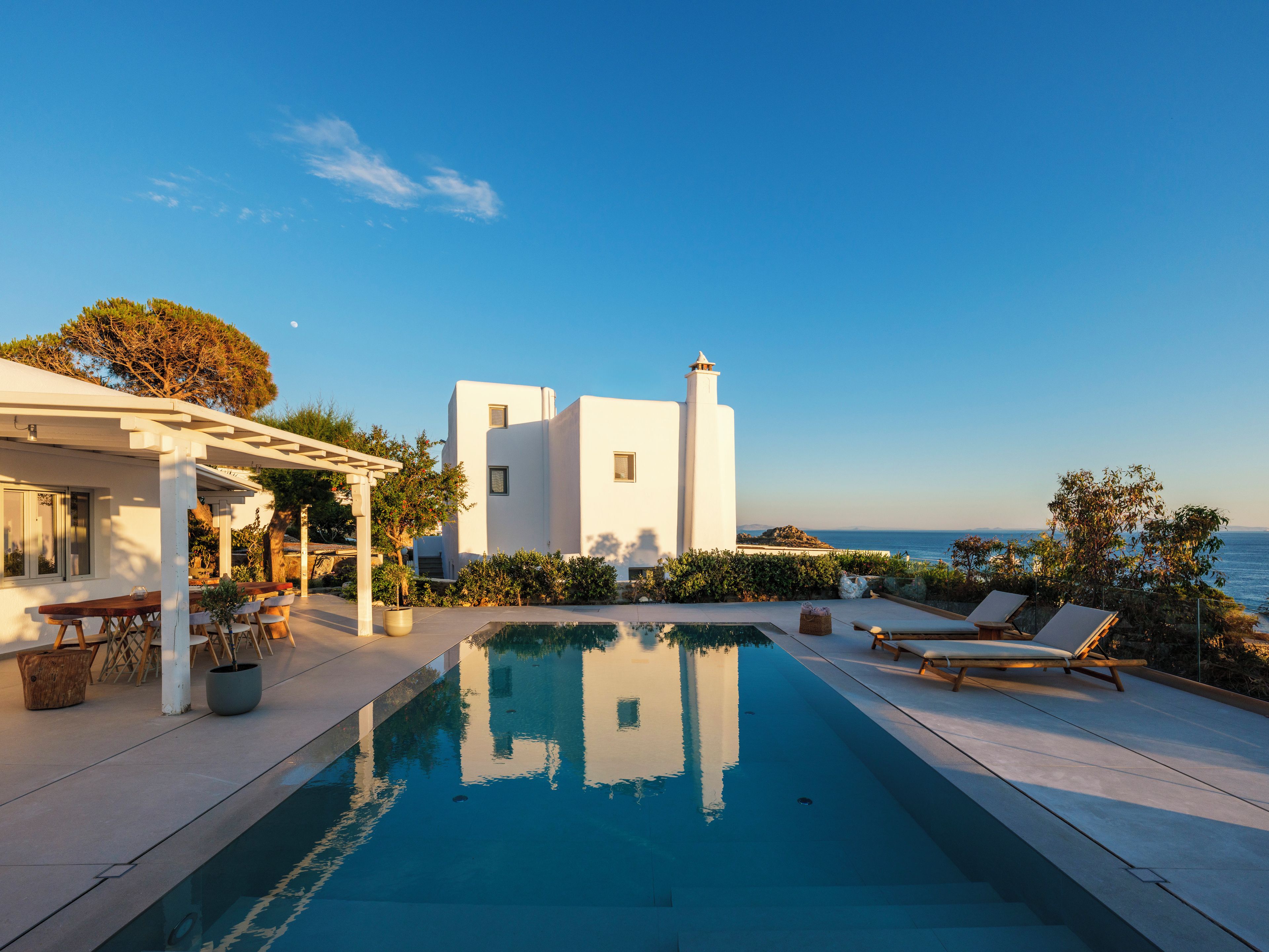 A modern villa with a swimming pool, outdoor seating, and a view of the sea.