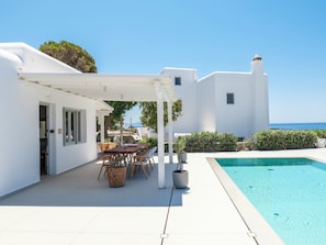 Un edificio blanco con piscina, mobiliario exterior y vistas al mar.