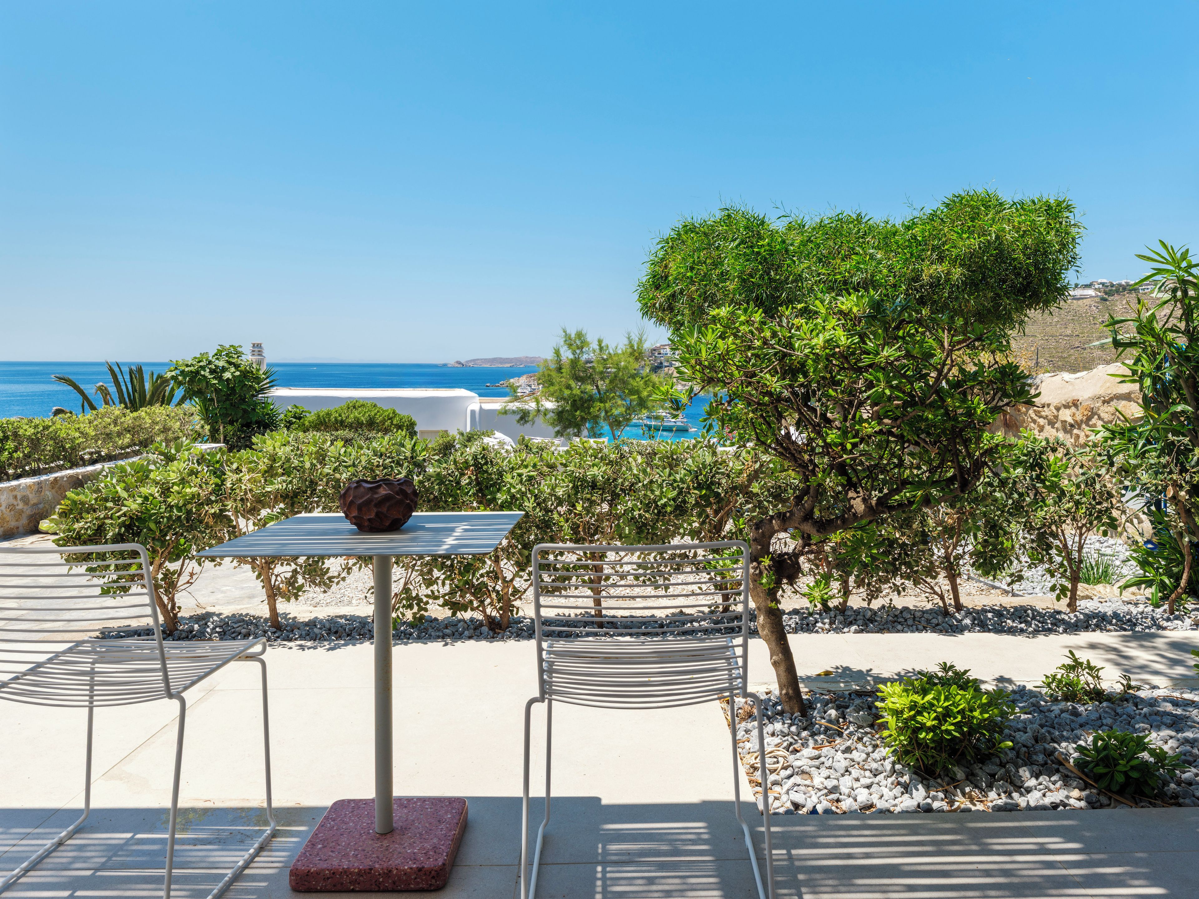 Un área de estar al aire libre con una mesa y sillas, un cuenco decorativo y vistas al mar y edificios al fondo.