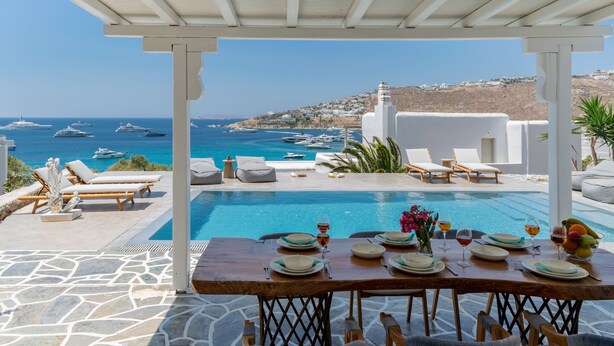 A poolside dining area with a view of the sea and boats. - MyMykonos Villa (Mykonos)