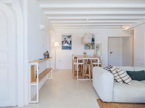Een moderne woonkamer met een witte bank, een eettafel met stoelen, een bankje en een hanglamp.