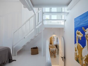 A spacious interior with a staircase leading to a loft area, a dining table, and a painting on the wall. - myMykonos Villa 1 (Mykonos)