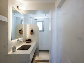 Un baño con lavamanos de mármol, un espejo y dos cestas de mimbre en la pared.