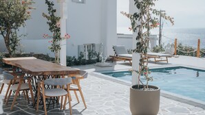 A poolside area with a wooden table and chairs, a potted plant, and a view of the sea. - MyMykonos Villa (Mykonos)