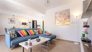 A modern living room with a blue sofa, colorful cushions, a white coffee table, and a large abstract painting on the wall. - Taurus - Deluxe Apartment with Sea View (Glyfada)