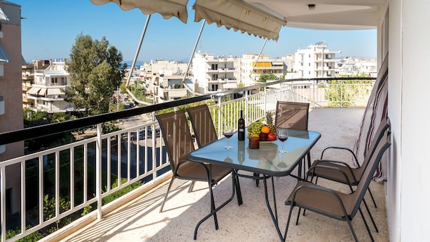 A balcony with a table, chairs, and a table setting including a bottle, glasses, and fruit. - Taurus - Deluxe Apartment with Sea View (Glyfada)