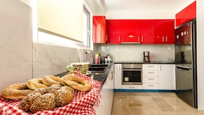 A modern kitchen with red cabinets, a stainless steel refrigerator, and a marble countertop. - Taurus - Deluxe Apartment with Sea View (Glyfada)