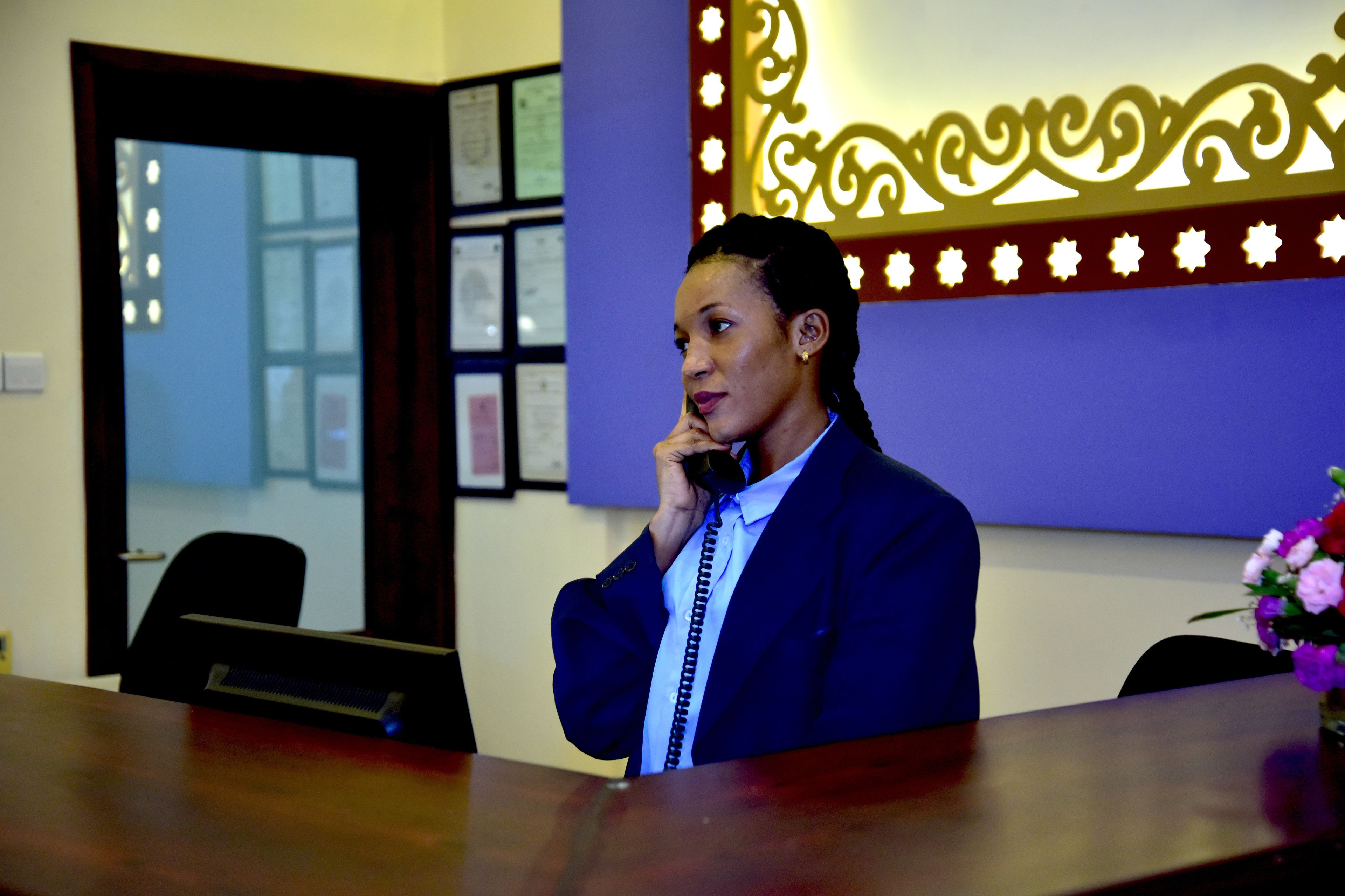 A person in a blue suit sitting at a desk with a telephone.