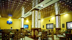 Un restaurant avec des chaises et des tables en bois, un téléviseur accroché au mur et des panneaux décoratifs au plafond.