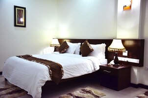 A neatly made bed with white and brown bedding, two bedside tables with lamps, and a framed picture on the wall.