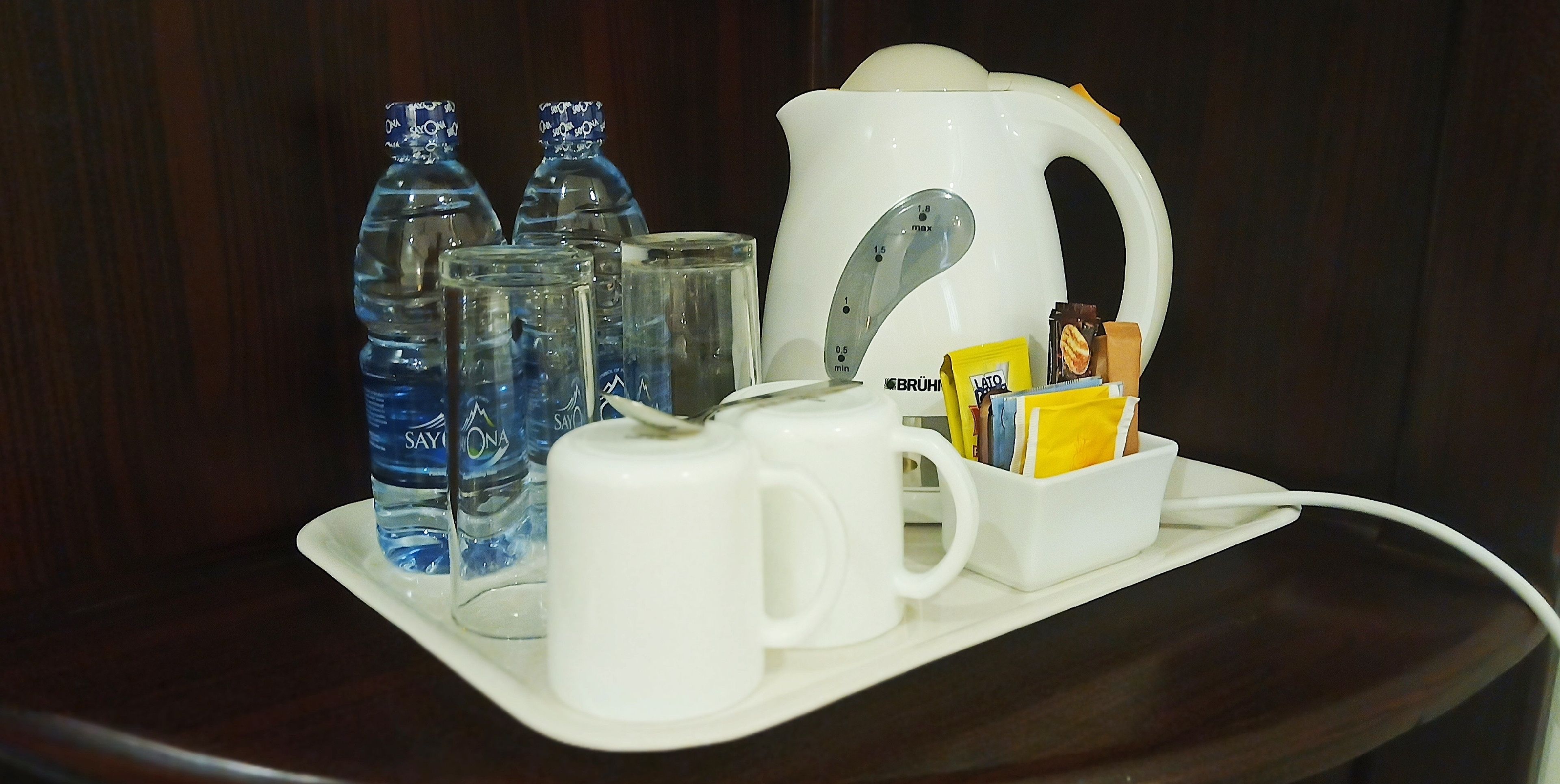 A tray with a white electric kettle, a white mug, and two glass bottles of water.