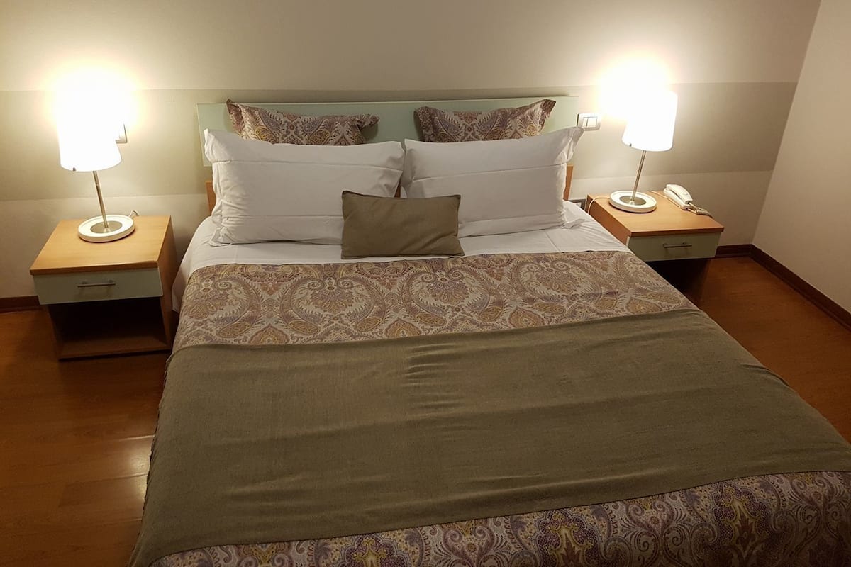 A neatly made bed with a patterned bedspread, two bedside lamps, and a bedside telephone on a wooden nightstand.