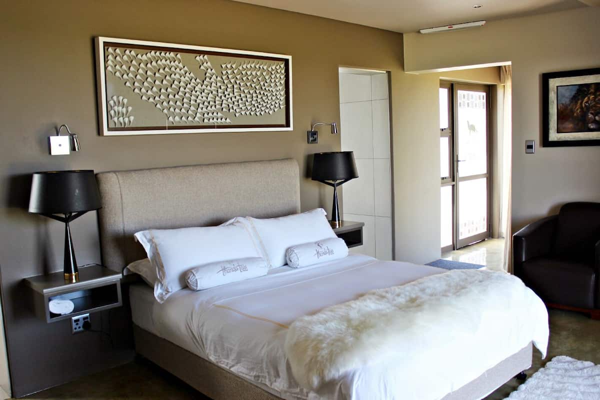 A bedroom with a large bed, two bedside tables, a headboard, a wall-mounted artwork, a door, and a chair.
