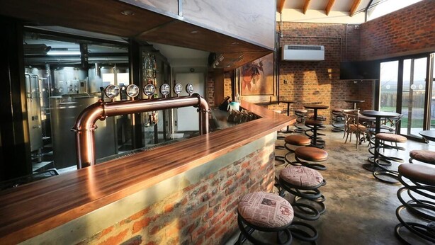 A bar area with a copper bar counter, stools, and a view of the kitchen in the background. - Thanda Tau - Hostel (Phumelela)