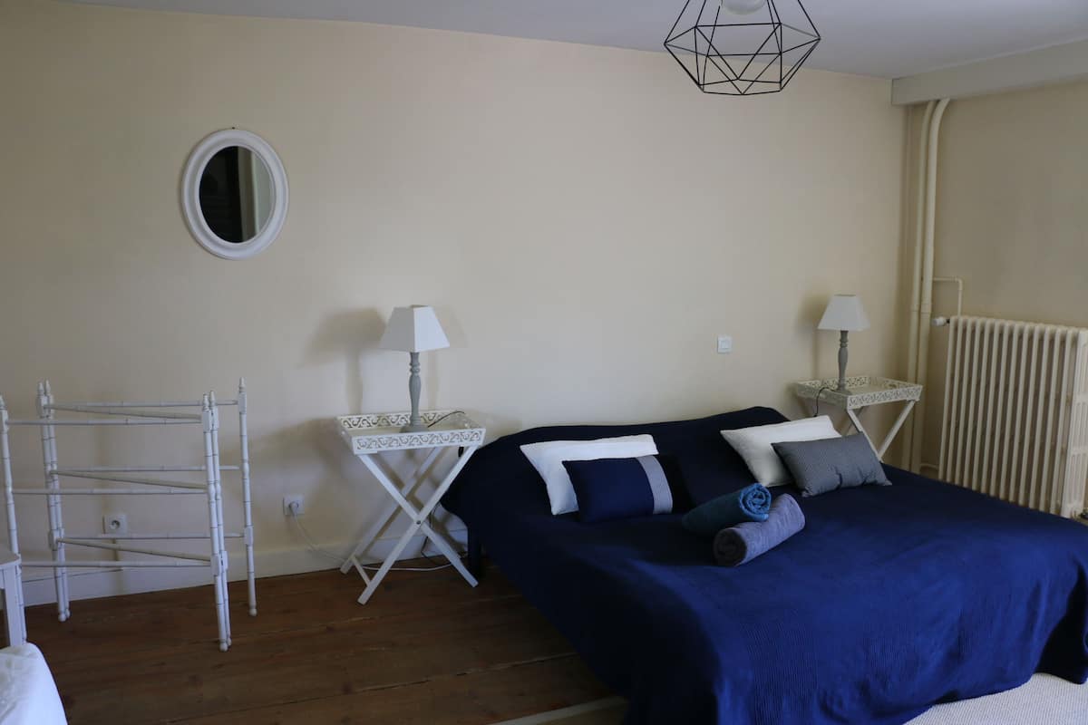 A bedroom with a bed, two bedside tables, a lamp, a radiator, and a wall-mounted shelf.