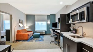 Une chambre d’hôtel moderne équipée d’une kitchenette, d’un canapé, d’un bureau et d’une grande fenêtre.