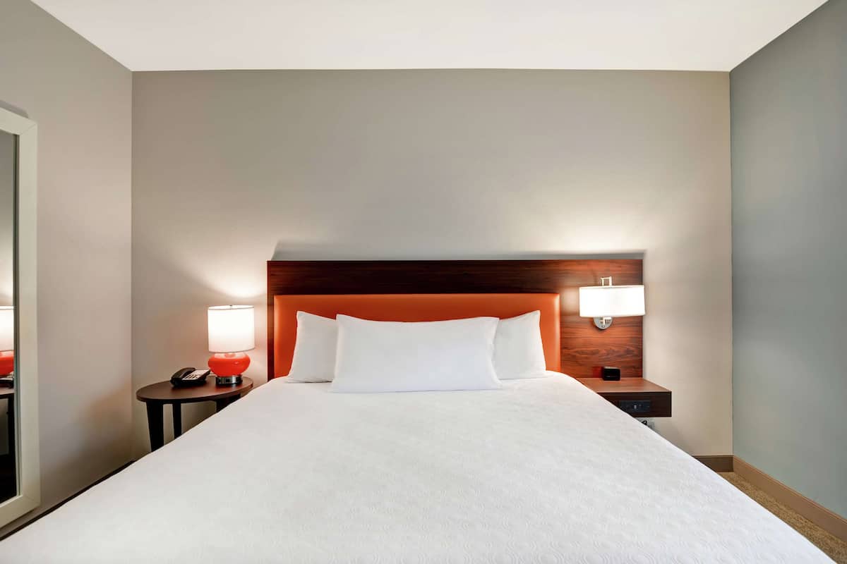 Hotellihuone, jossa on suuri sänky, kaksi yöpöytää valaisimineen ja puinen pääty.