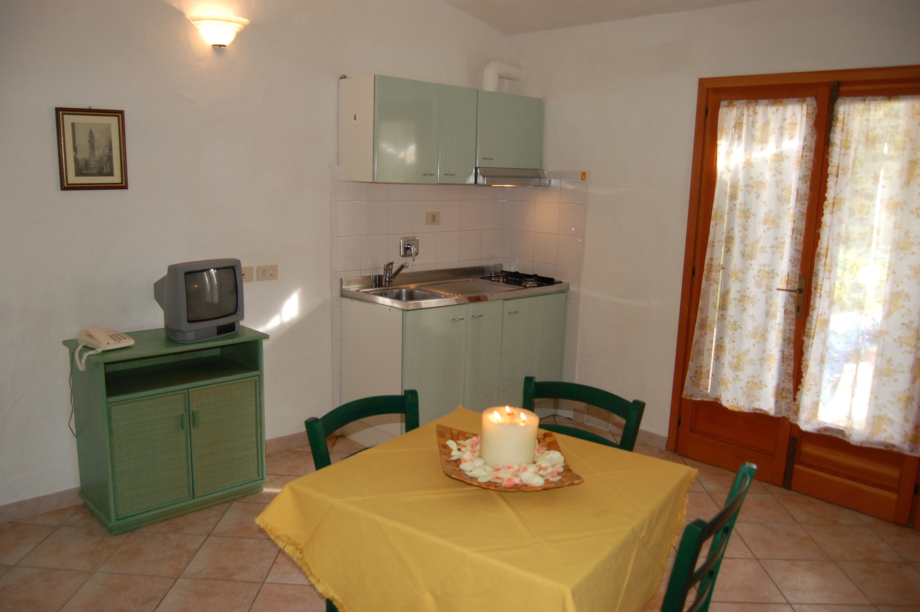 A compact kitchen with a sink, stove, and green cabinets. There is a dining table with chairs and a candle centerpiece.
