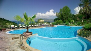 A swimming pool with lounge chairs and a palm tree, surrounded by greenery and a mountainous backdrop. - Villaggio Innamorata - Villa Gisella (Capoliveri)
